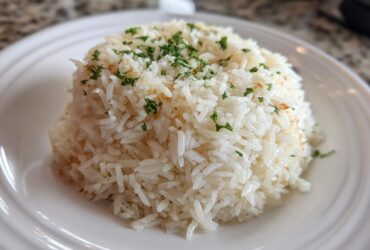 A mound of fluffy, white rice pilaf garnished with chopped fresh parsley served on a white plate.