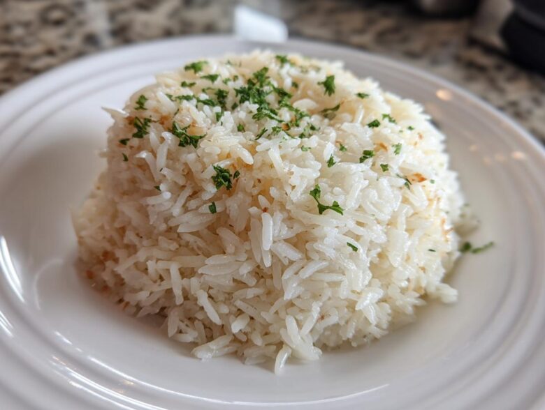 A mound of fluffy, white rice pilaf garnished with chopped fresh parsley served on a white plate.