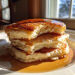 Close-up of a stack of fluffy sourdough discard pancakes dripping with golden syrup.