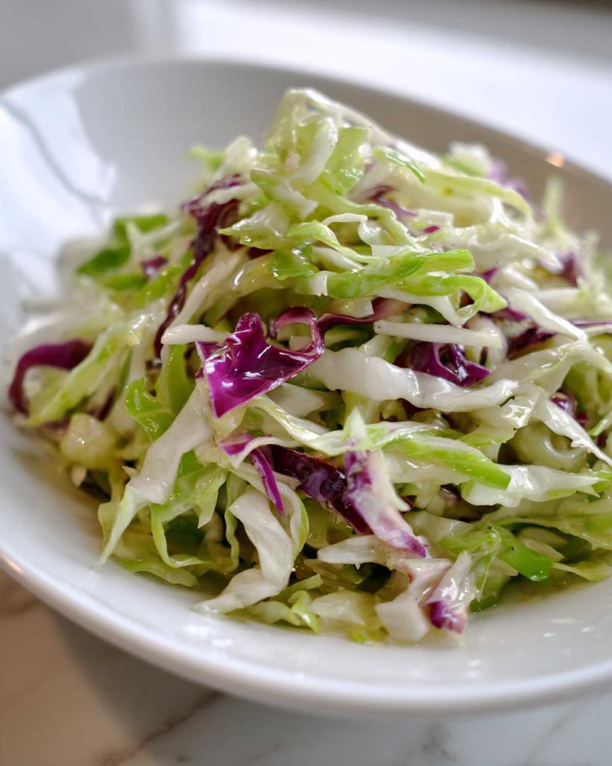Close-up of a vibrant cabbage salad featuring shredded green and purple cabbage lightly dressed.