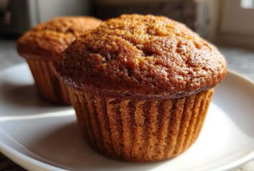 Close-up of two golden-brown, freshly baked honey bran muffins sitting on a white plate.