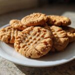A stack of golden brown peanut butter cookies with classic crosshatch fork marks on a white plate.