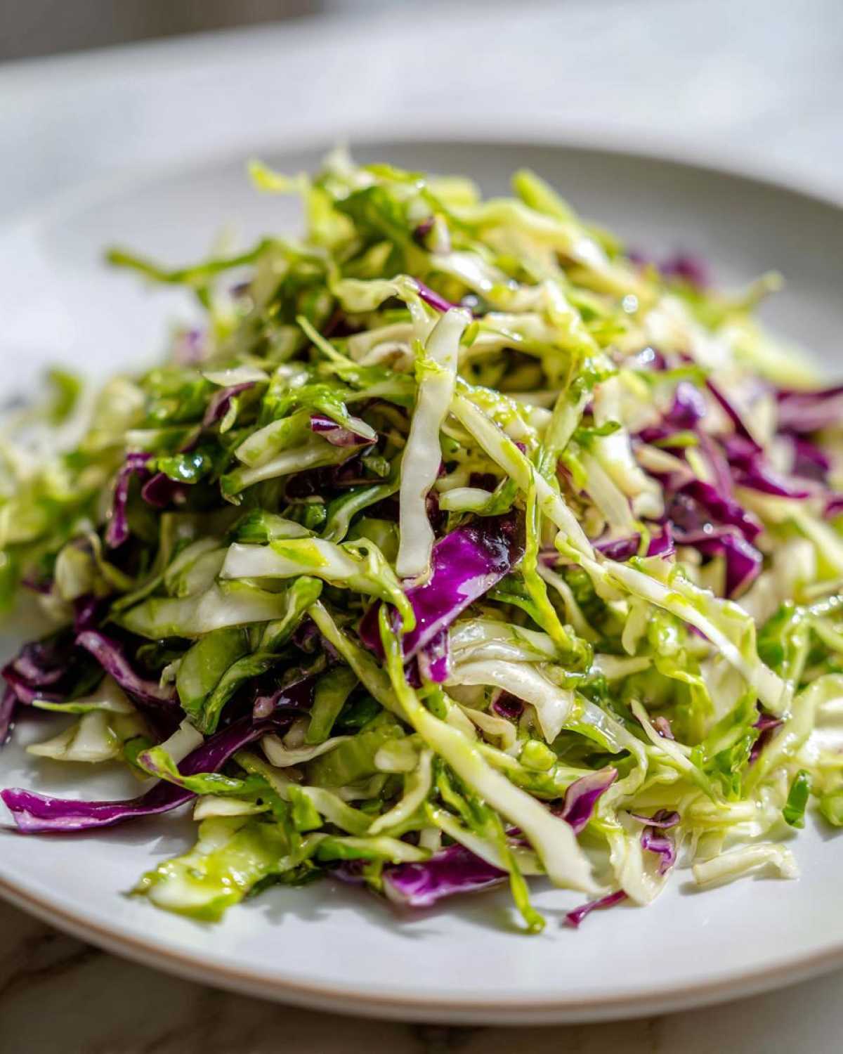 Close-up of a mound of vibrant, shredded cabbage salad featuring green and purple cabbage.