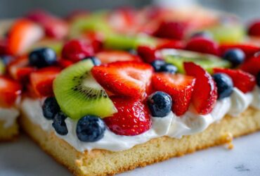 A close-up view of a slice of fruit pizza sugar cookie topped with cream cheese frosting and fresh berries.