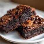 Close-up of two fudgy sweet potato brownies topped with melted chocolate chips on a white plate.