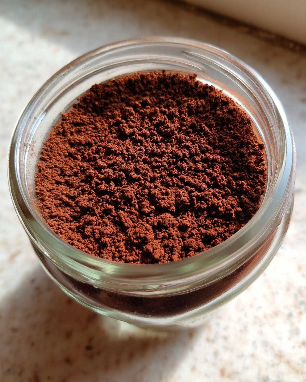 Close-up overhead shot of rich brown powder, likely cocoa, stored in a small glass jar for making hot cocoa mix.