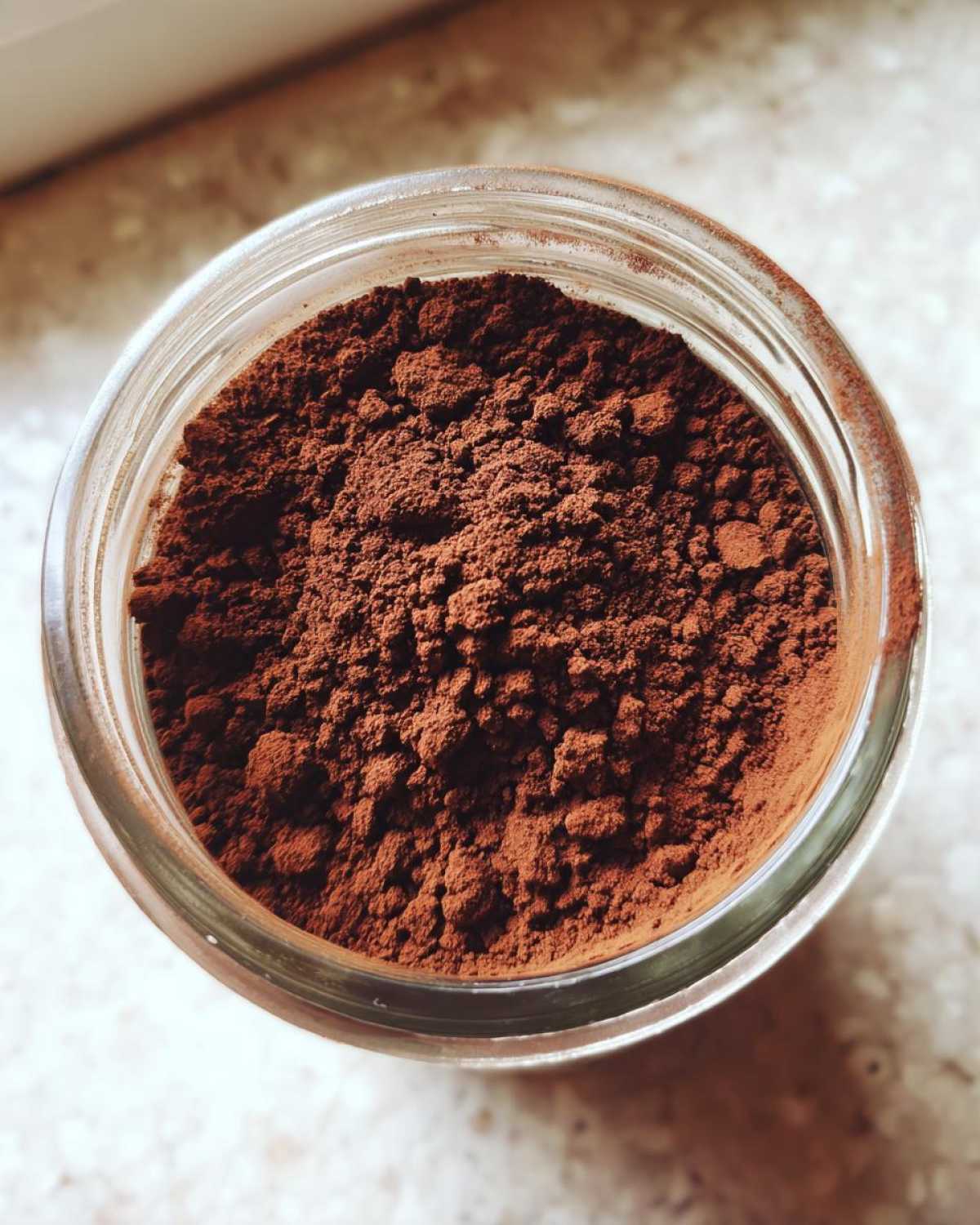 Overhead close-up view of rich brown homemade hot cocoa mix powder filling a clear glass jar.