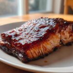 Close-up of a perfectly cooked, glazed salmon fillet resting on a white plate.