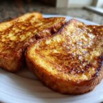 Close-up of two thick slices of golden brown french toast served on a white plate.