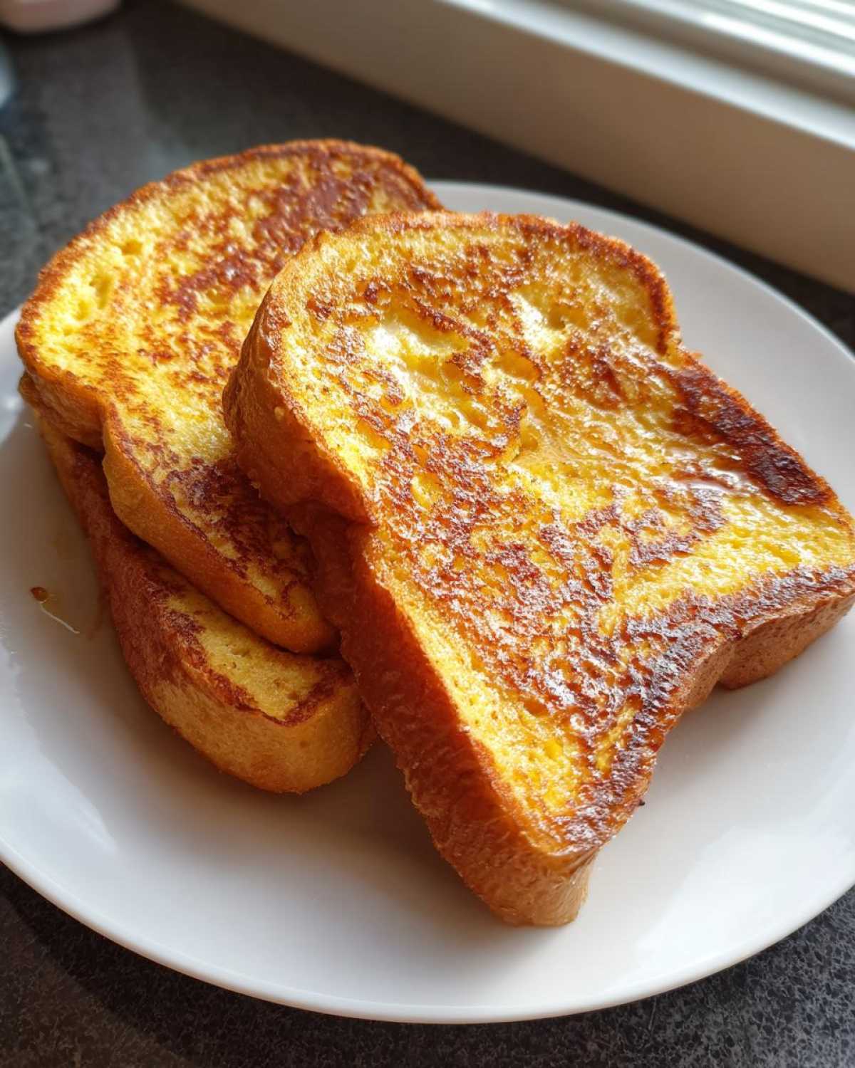 Three golden-brown slices of perfectly cooked french toast stacked slightly on a white plate.