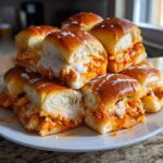 A stack of gooey, cheesy buffalo chicken sliders on a white plate, featuring shredded chicken and melted white cheese.