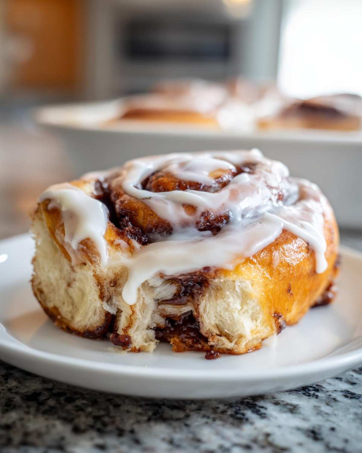 A gooey, freshly baked cinnamon roll topped with thick white icing, with a bite taken out to show the soft interior.