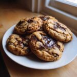 A stack of five freshly baked homemade chocolate chip cookies with melted chocolate pools on a white plate.