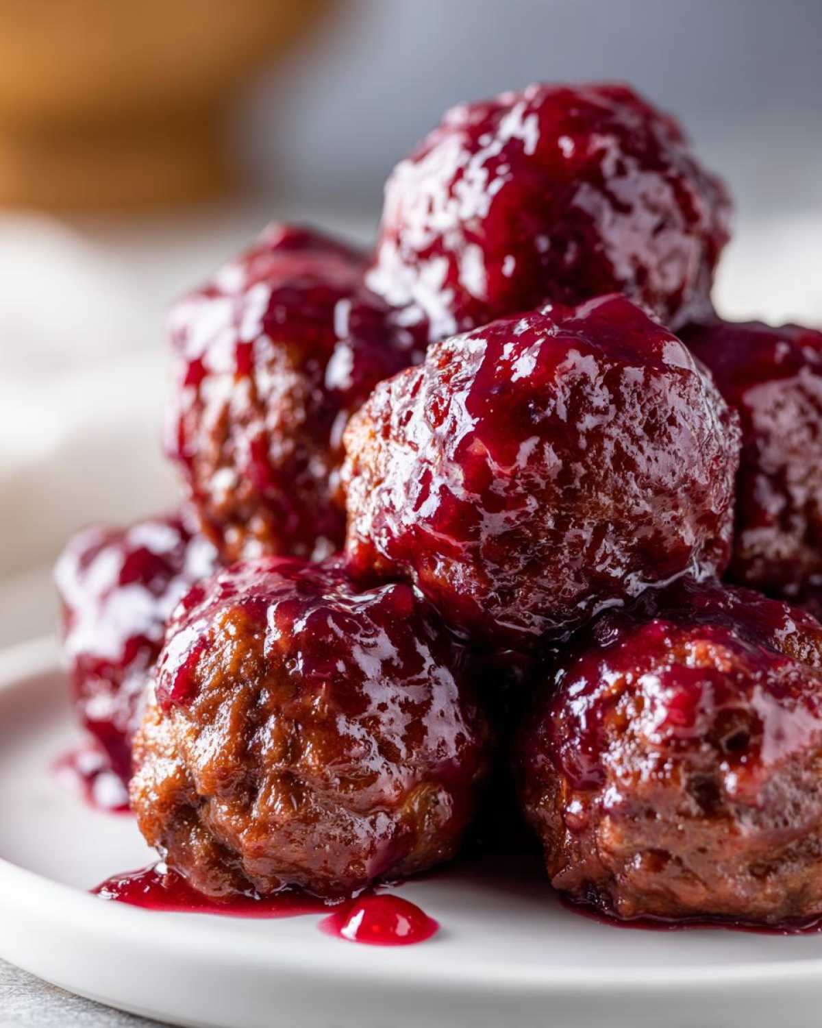 A close-up of several savory Grape jelly meatballs piled high and coated in a thick, glossy, dark red grape jelly glaze.