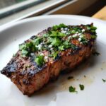 Close-up of a perfectly grilled steak, likely prepared with carne asada marinade, topped with fresh cilantro and flaky salt.