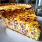 A close-up slice of golden baked ham and cheese quiche showing diced ham in the creamy egg filling.
