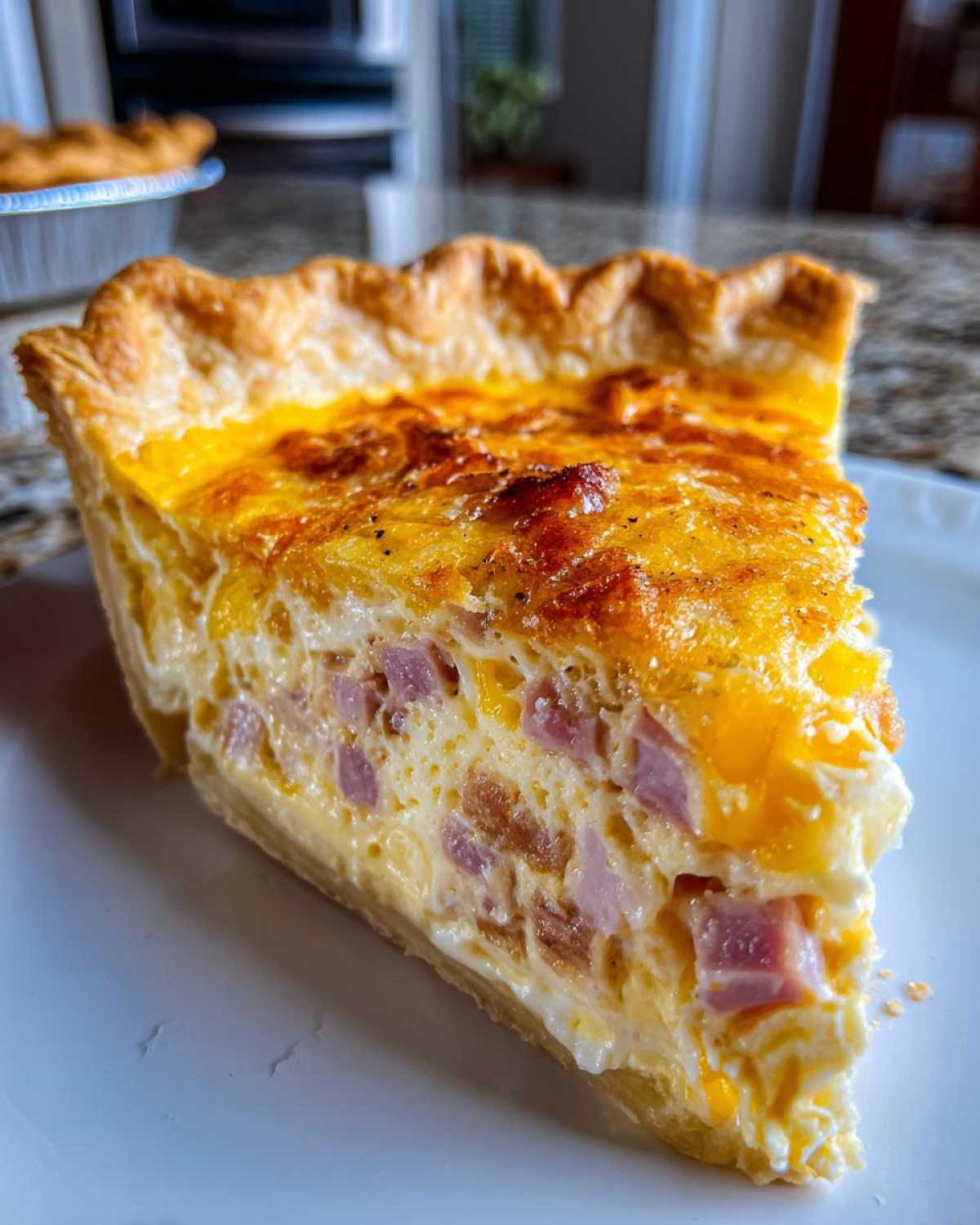 A close-up of a thick slice of Ham and Cheese Quiche showing a flaky crust and creamy filling packed with ham cubes.