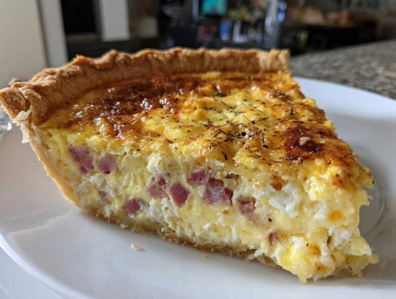 A close-up of a thick slice of Ham and Cheese Quiche with a golden-brown top, served on a white plate.