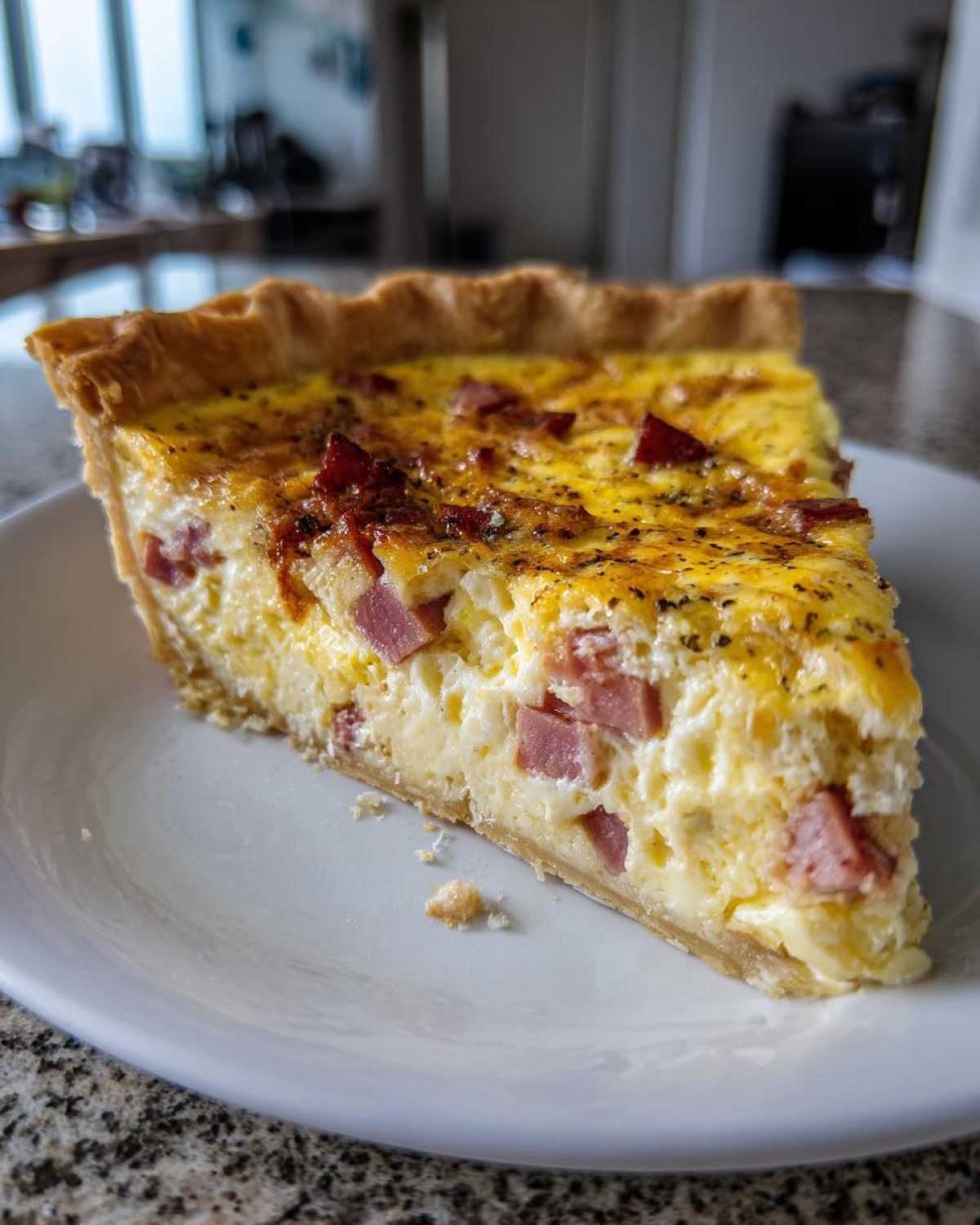 A close-up of a perfect slice of ham and cheese quiche showing the creamy filling and golden crust.