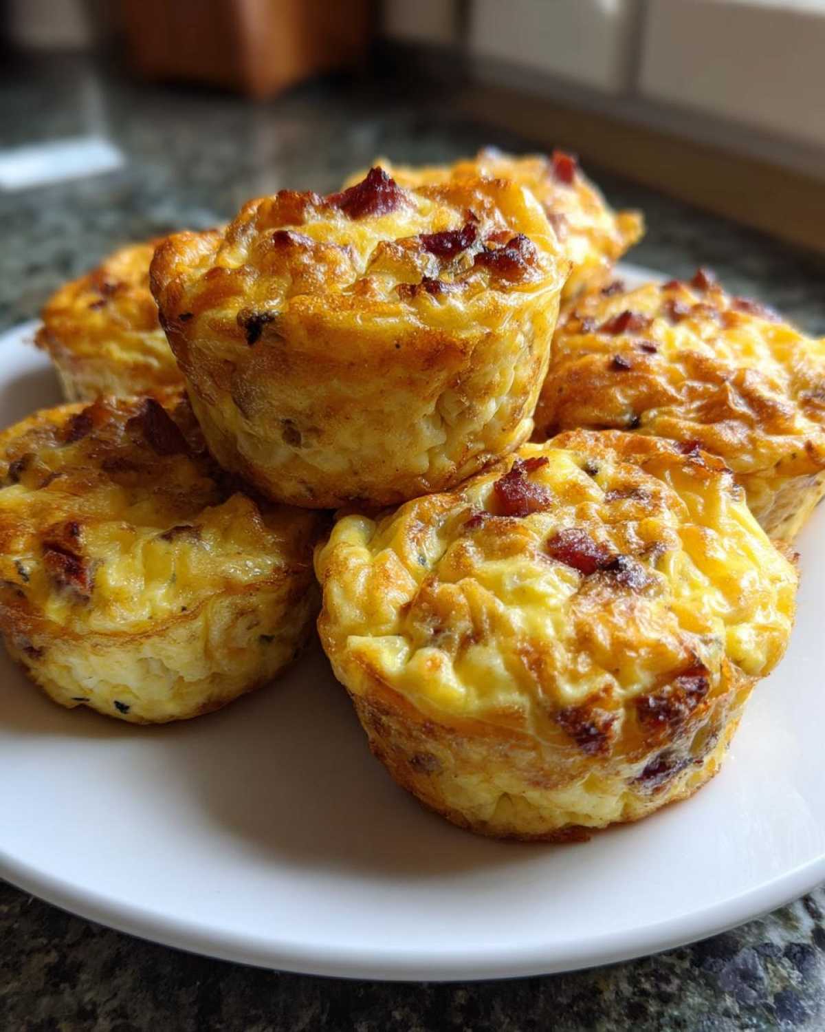 A stack of freshly baked, golden brown, high-protein egg bites topped with crispy bacon pieces.