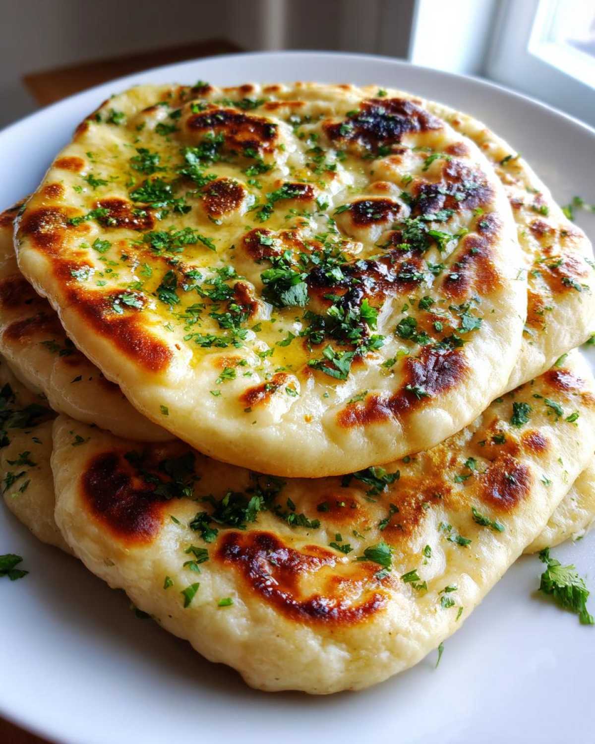 A close-up stack of freshly cooked homemade naan bread brushed with melted butter and topped with chopped fresh parsley.