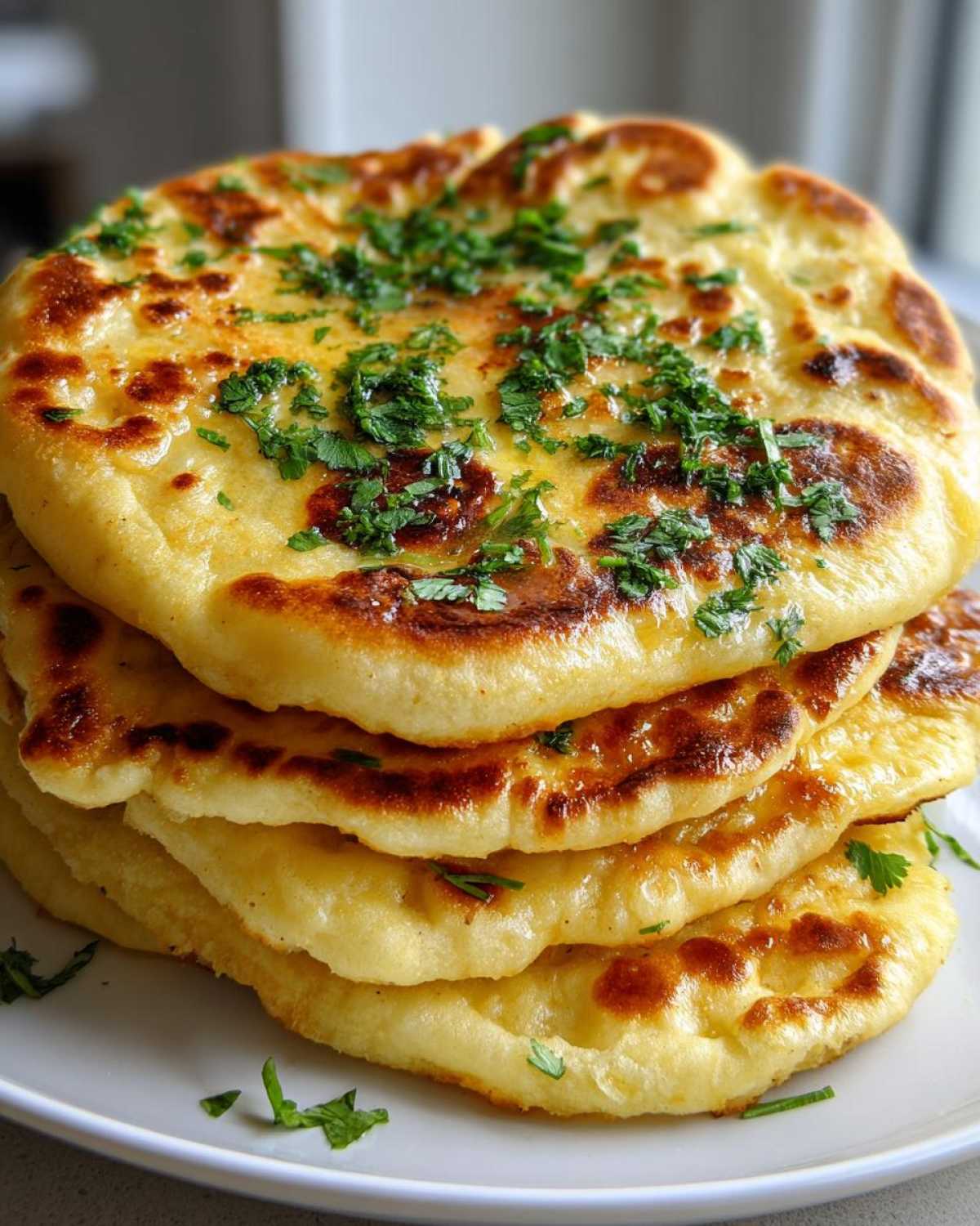 A stack of four golden-brown homemade naan bread rounds, brushed with butter and topped with fresh chopped cilantro.