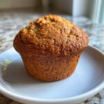 A single, golden-brown honey bran muffin sitting on a small white plate.