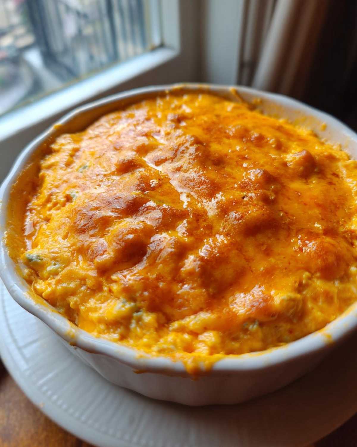 Close-up of hot, bubbly Buffalo chicken dip topped with melted orange cheese in a white serving bowl.