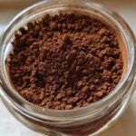 Overhead close-up of rich brown homemade hot cocoa mix powder filling a clear glass jar.