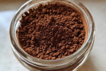 Overhead close-up of rich brown homemade hot cocoa mix powder filling a clear glass jar.