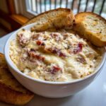 Close-up of hot, cheesy reuben dip topped with melted cheese and served with toasted bread slices.