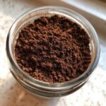 Overhead close-up of rich, dark brown homemade hot cocoa mix powder stored in a clear glass jar.