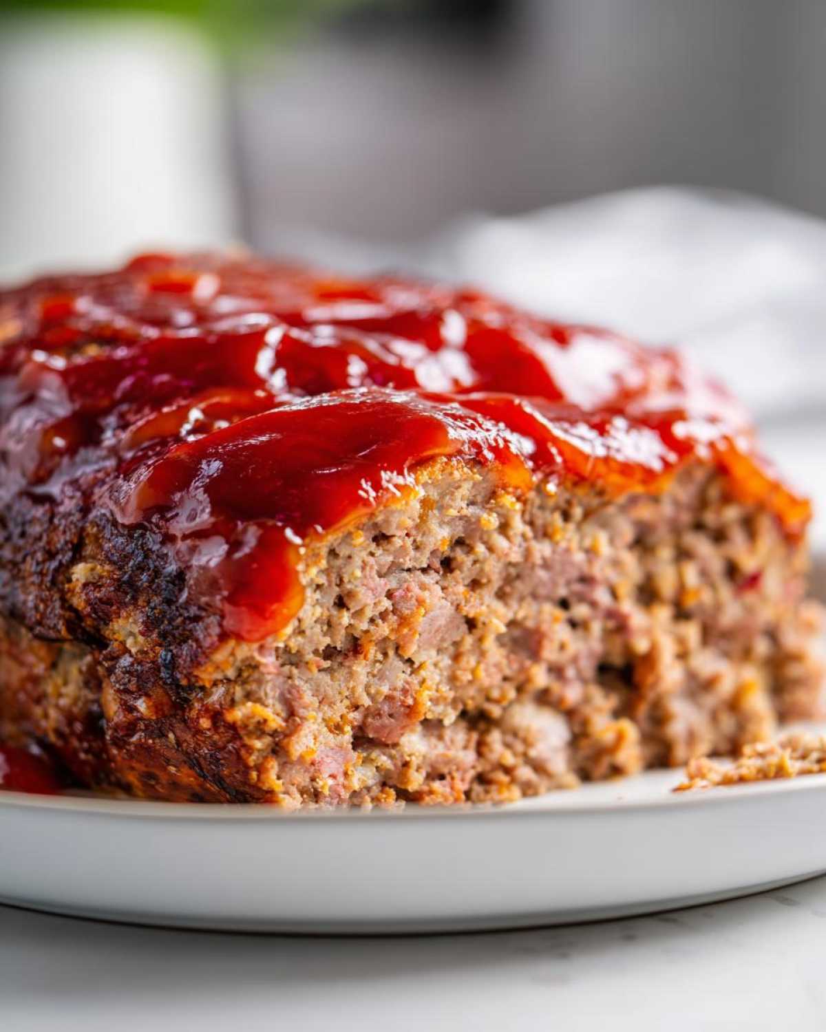 Close-up of a freshly baked meatloaf with a thick, glossy red glaze, showing the moist texture inside.