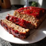 Close-up of a sliced, juicy meatloaf topped with a thick, glossy red glaze.