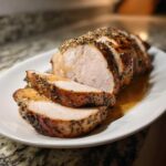 Close-up of a juicy pork loin roast, sliced and drizzled with pan juices, showing a flavorful herb crust.
