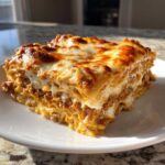 A perfect square slice of Lasagna with Cottage Cheese showing layers of pasta, meat sauce, and melted, browned cheese on top.