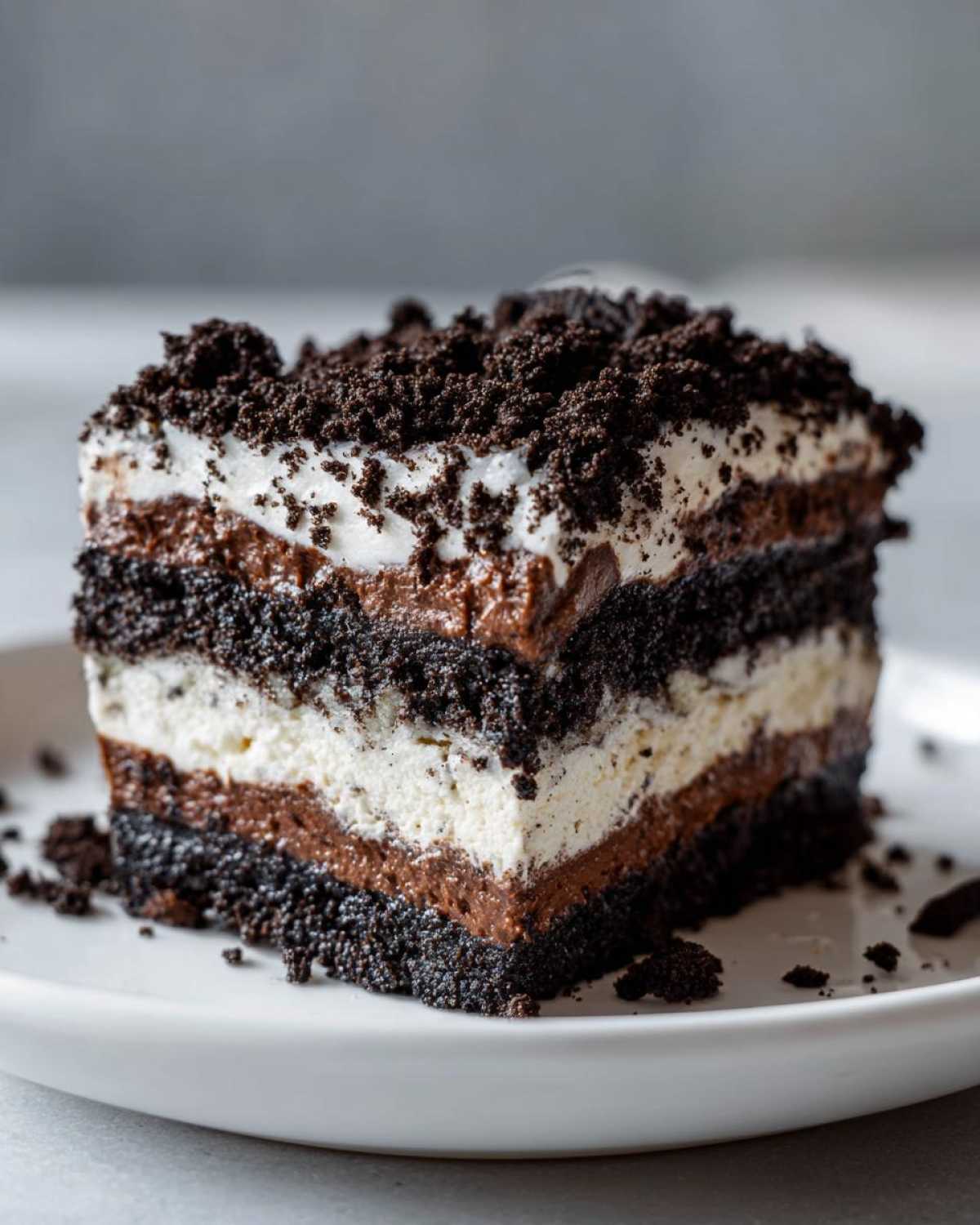 Close-up of a thick, layered slice of Oreo dirt cake showing alternating layers of dark cookie crumbs, white cream, and chocolate pudding.