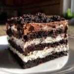 A rich, layered slice of oreo dirt cake featuring alternating chocolate cookie crumbs and white cream filling.