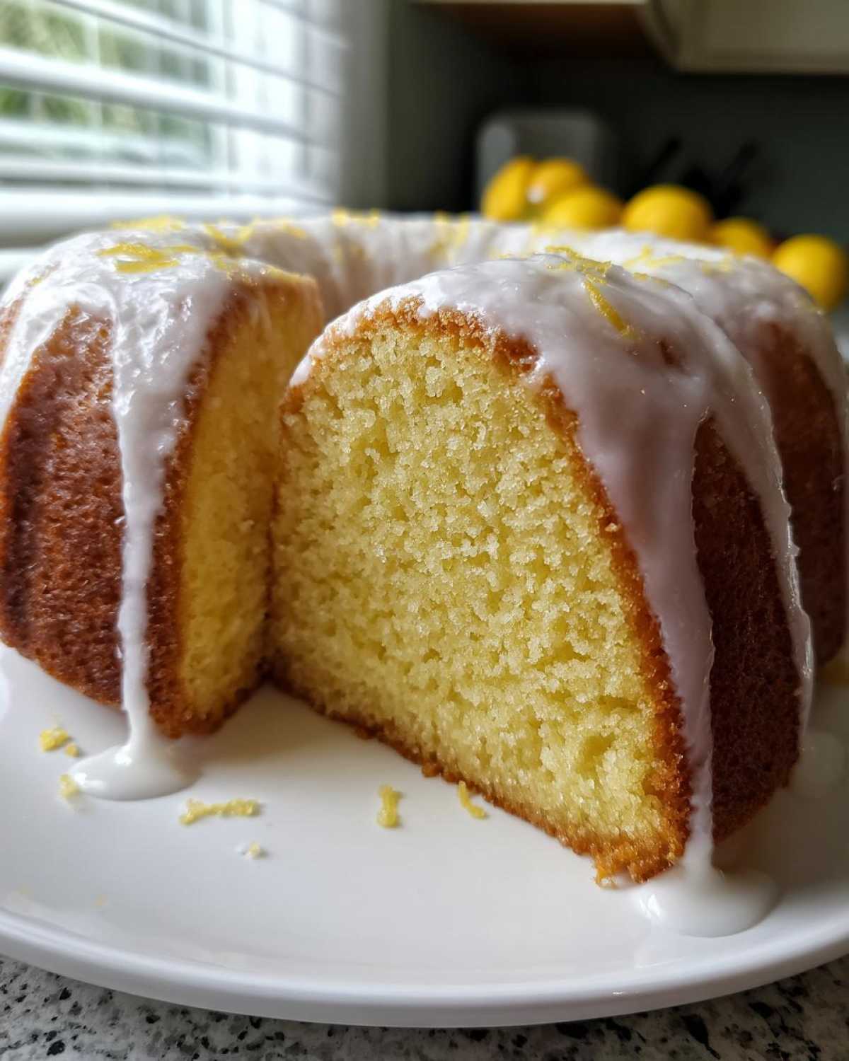 Close-up of a slice cut from a moist lemon pound cake drizzled with white glaze and lemon zest.