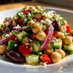 Close-up of a vibrant Mediterranean bean salad featuring chickpeas, cucumber, red onion, olives, and feta cheese.