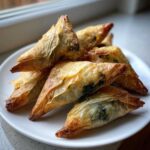 A pile of golden brown, crispy Mediterranean Spinach and Feta Cheese Crisps served on a white plate.