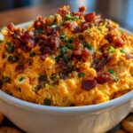 A close-up of creamy, orange-colored million dollar dip topped generously with crispy bacon bits and chopped green onions.