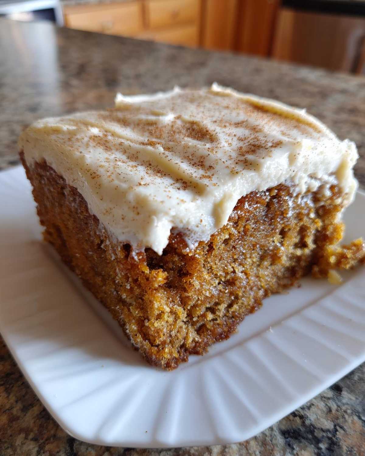 A close-up of a moist slice of applesauce cake topped with thick cream cheese frosting and sprinkled with cinnamon.