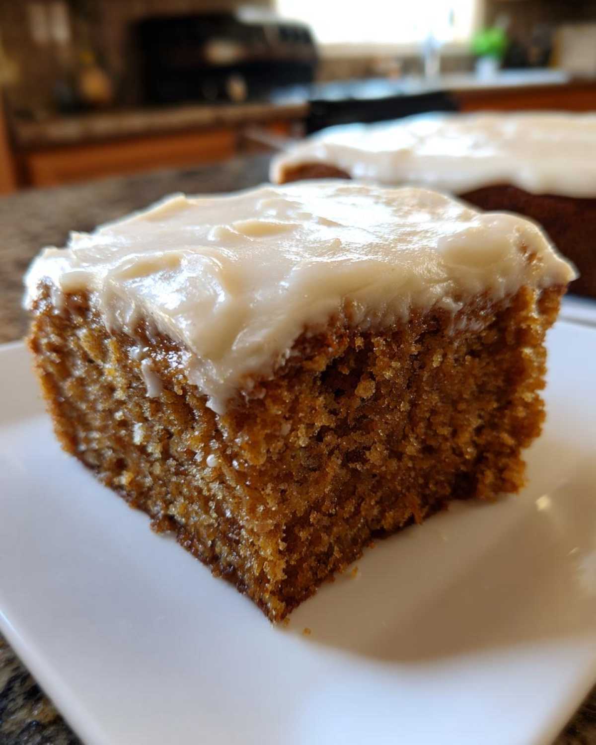 Close-up of a square slice of moist, spiced applesauce cake topped with thick, white frosting.