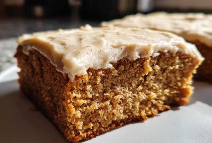 Close-up of a moist slice of applesauce cake topped with thick, creamy frosting dusted with spice.
