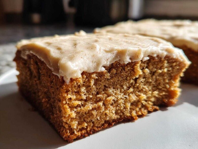 Close-up of a moist slice of applesauce cake topped with thick, creamy frosting dusted with spice.