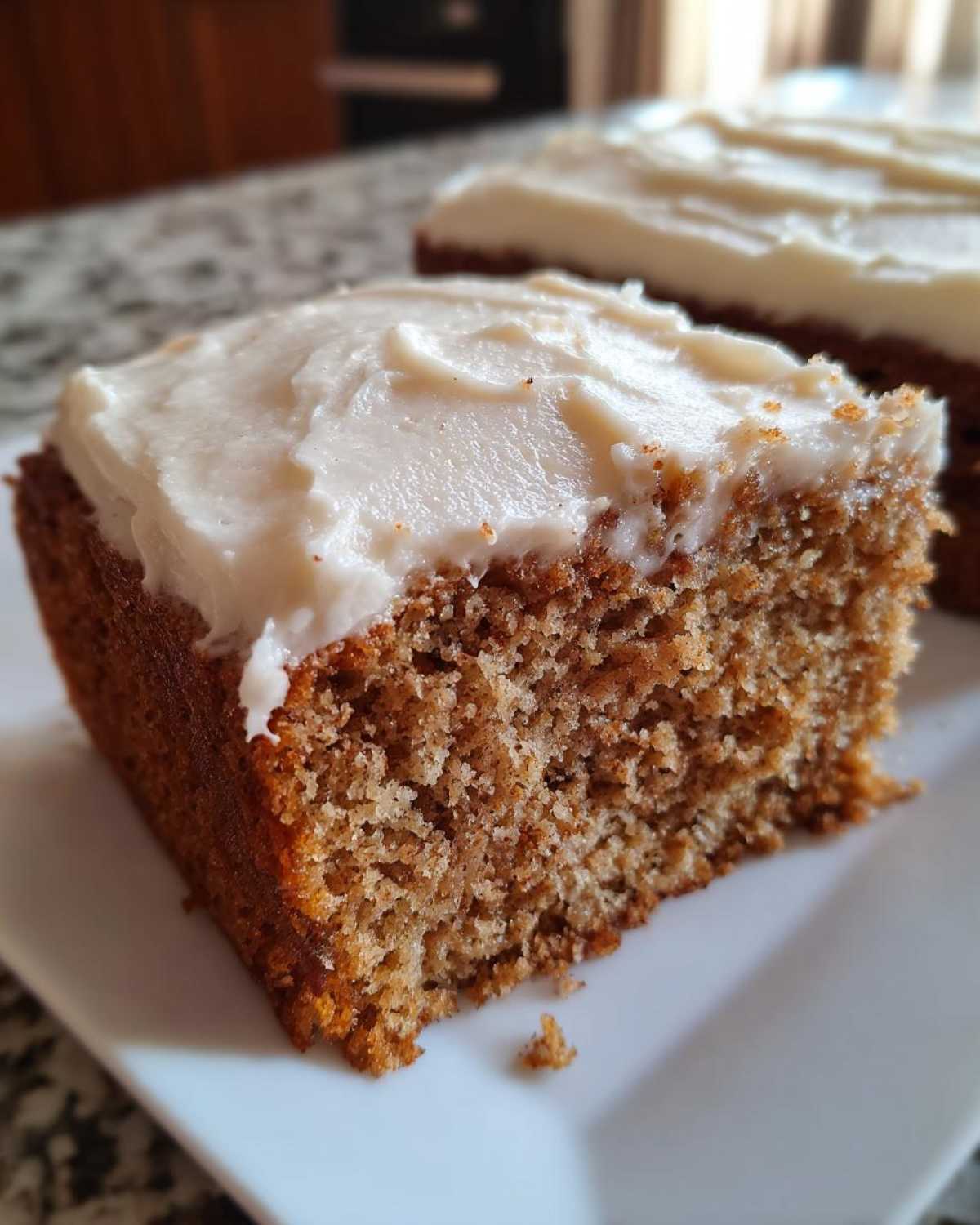Close-up of a moist slice of applesauce cake topped with thick, white frosting.