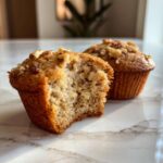 Close-up of a moist banana nut muffin with a bite taken out, revealing the soft interior and walnuts.