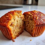 Close-up of a moist banana nut muffin cut in half, showing the soft interior texture and nuts.