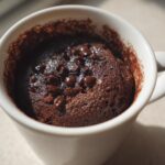Close-up of a freshly baked chocolate mug cake topped with chocolate chips inside a white mug.